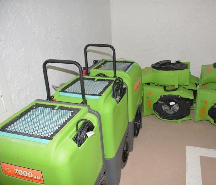 Green SERVPRO equipment sitting in a water damaged room with white walls.